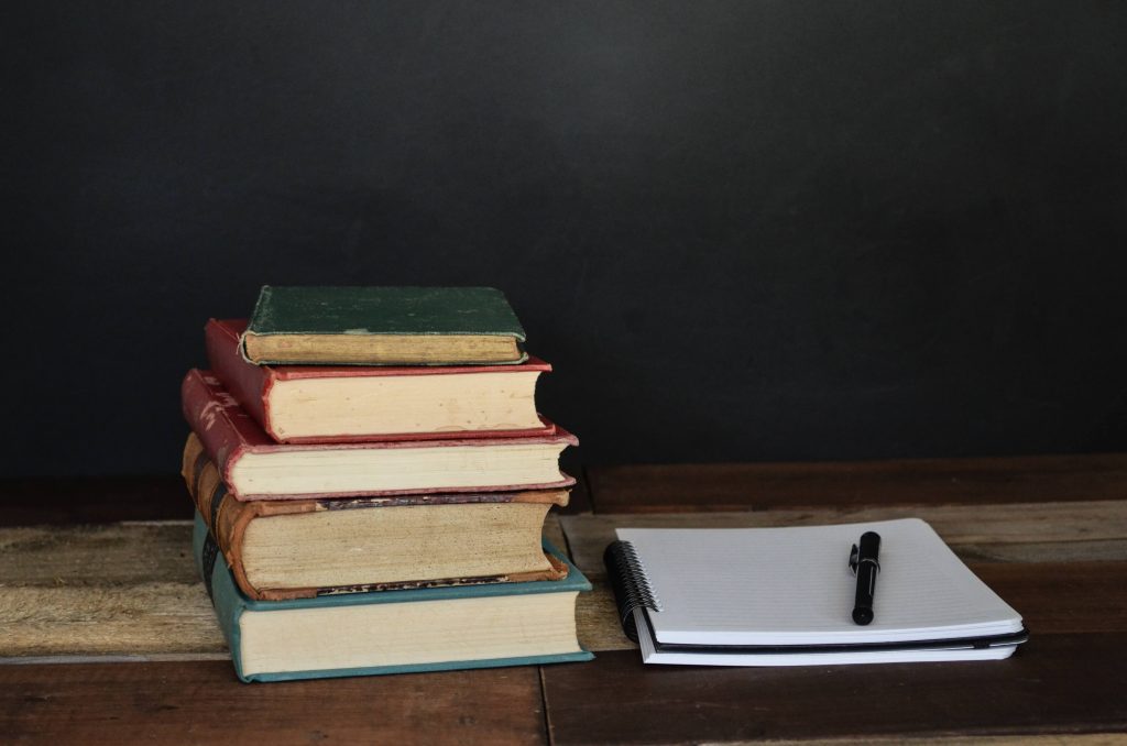 pilha de livros à esquerda e, à direita, caderno com caneta em cima