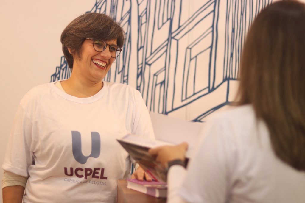 Colaboradora da UCPel sorri utilizando a camiseta com a nova identidade visual.