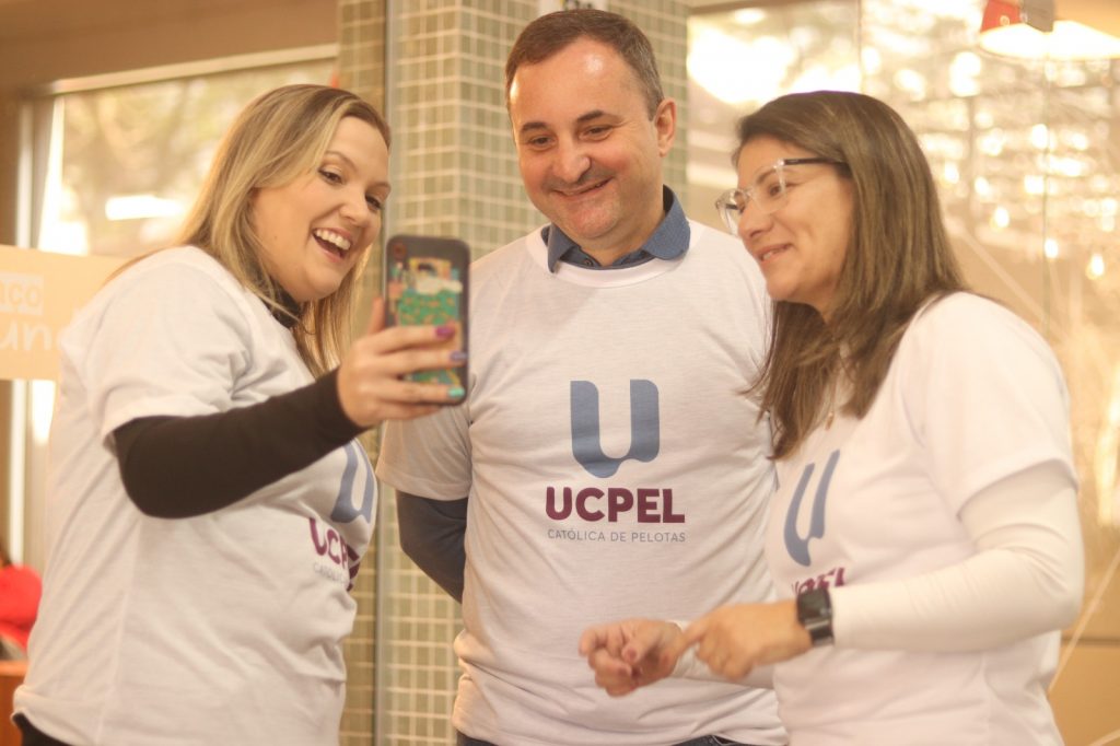 Aluna e professores da UCPel conversam utilizando a camiseta com a nova identidade visual.