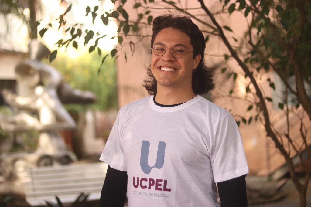 Aluno da UCPel sorri utilizando a camiseta com a nova identidade visual.